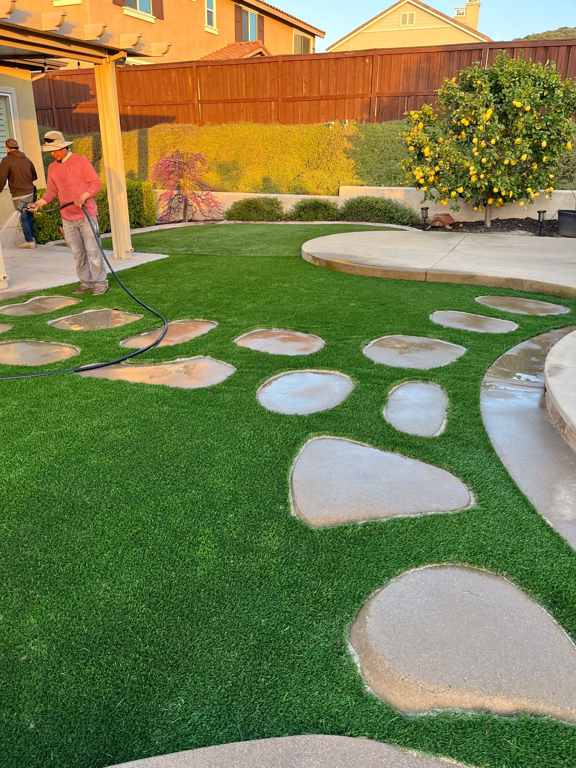 A woman is mowing the grass in a backyard with stepping stones.
