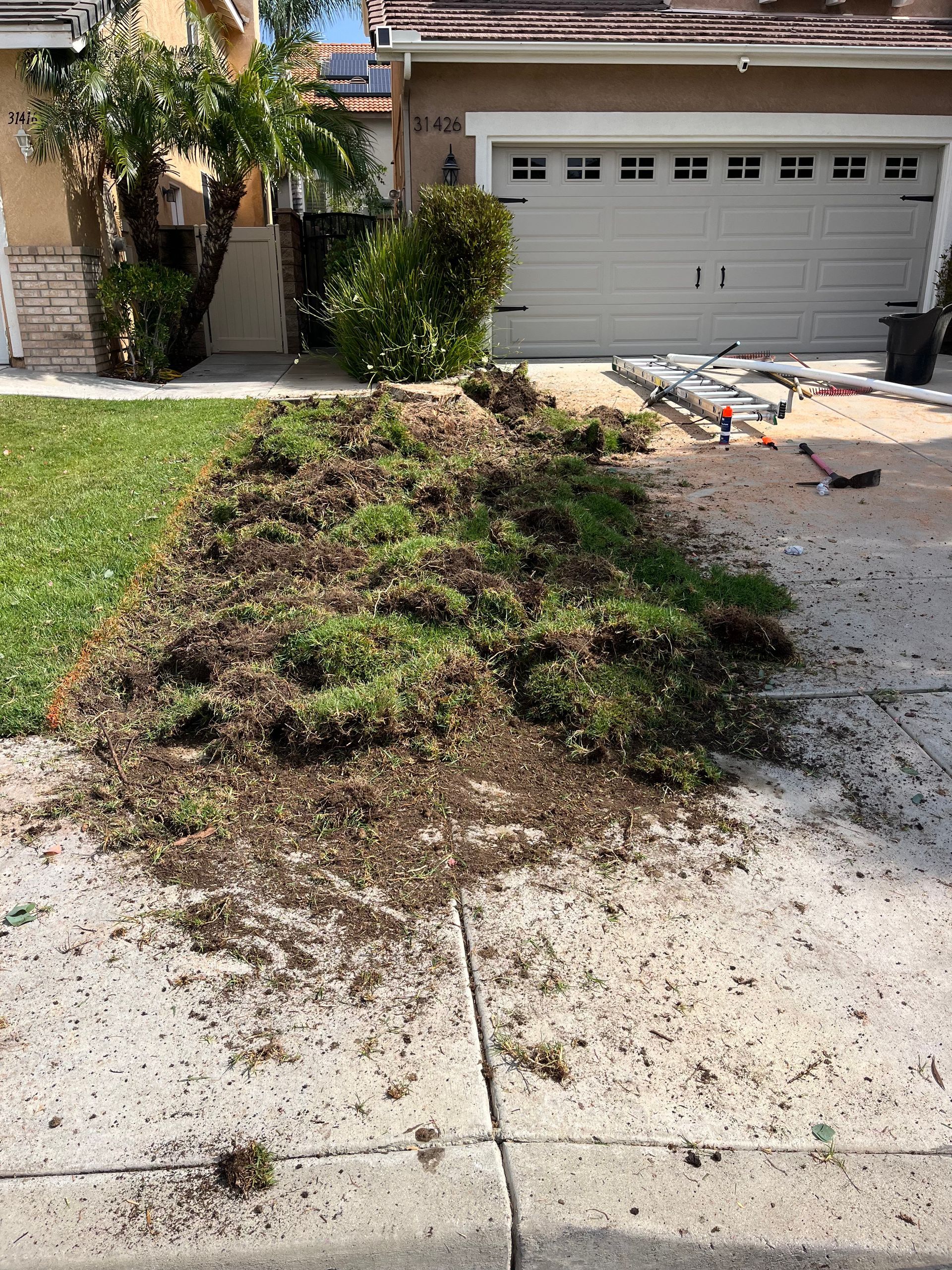 Front yard with a large uprooted grass on a driveway beside a garage, with debris scattered nearby.