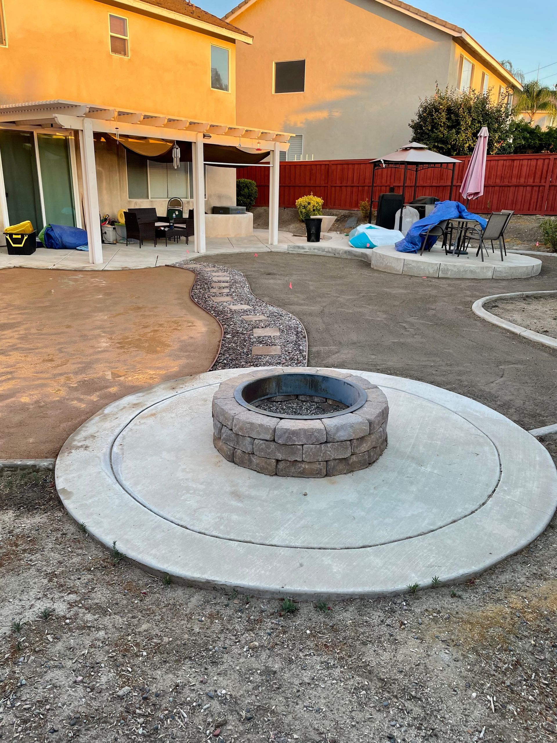 Backyard with fire pit on concrete pad, patio, and partially landscaped areas.