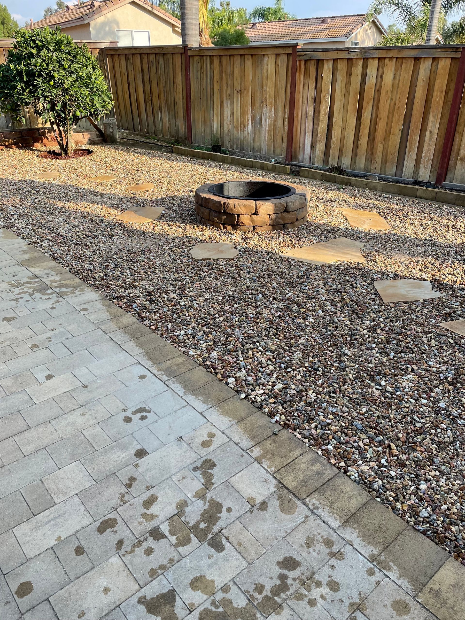 Patio with cobblestone pavers, gravel, fire pit, and wooden fence.