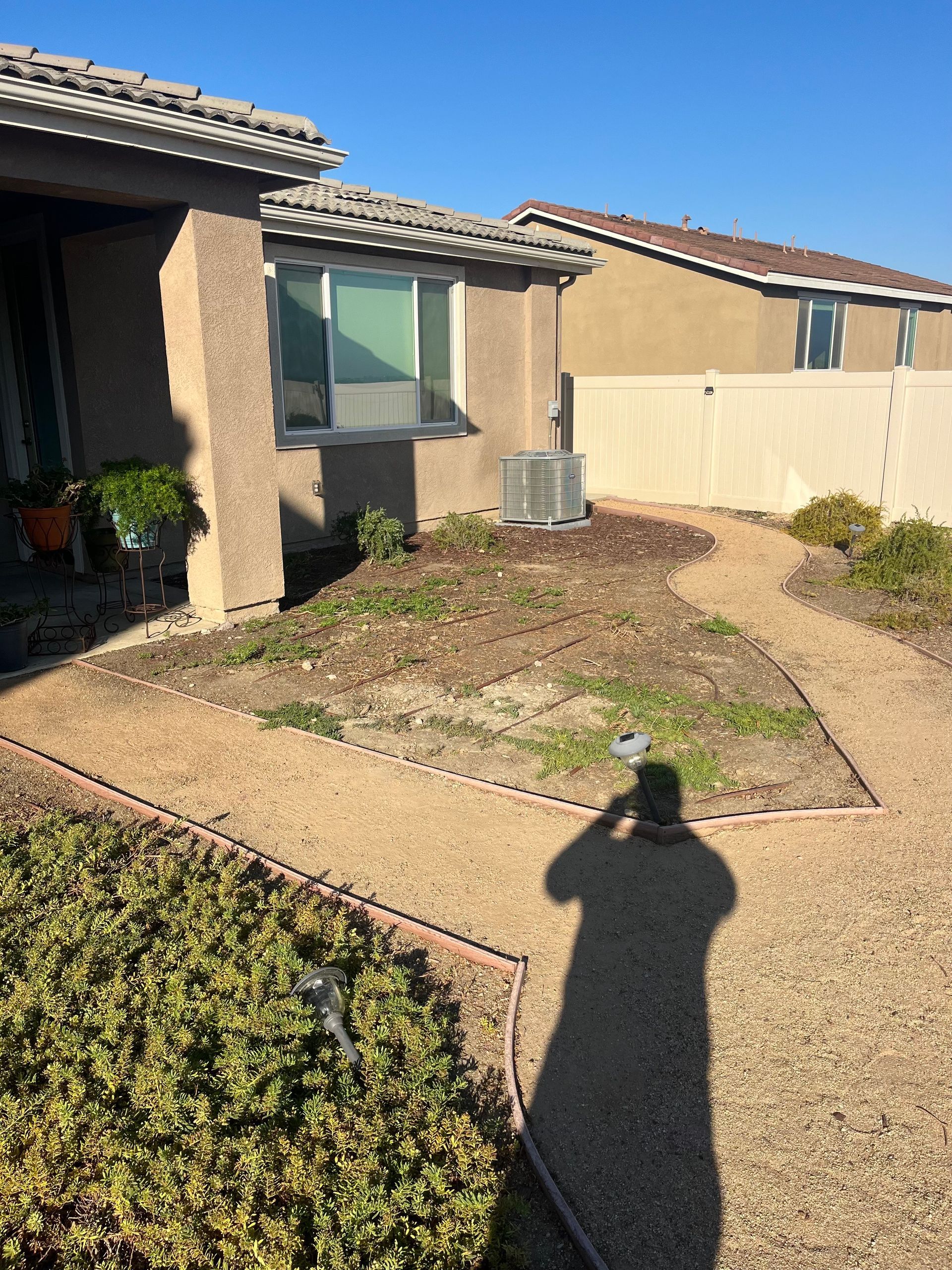 A shadow of a person is cast on a gravel path in front of a house.