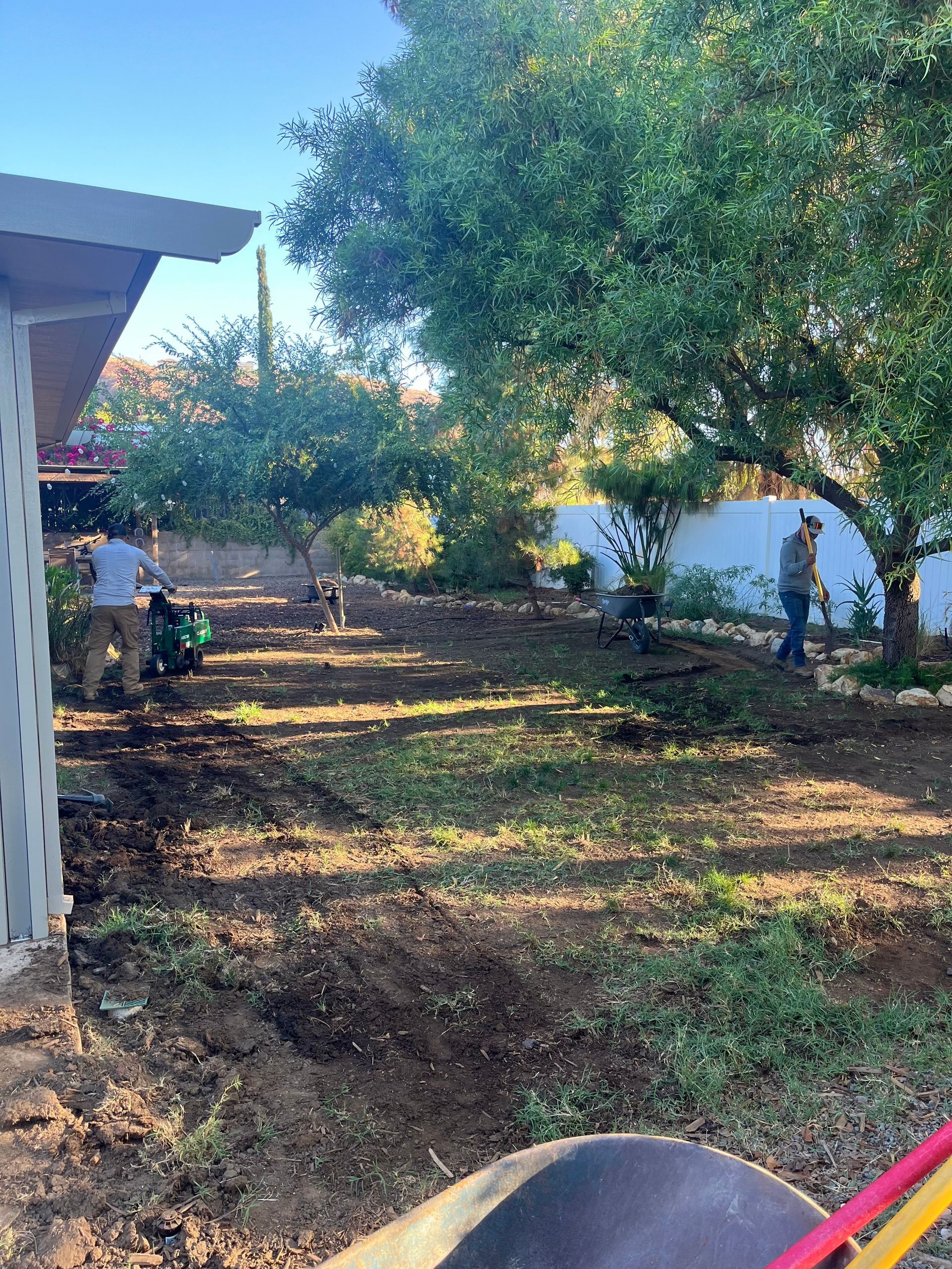 A man is digging in a yard with a wheelbarrow.