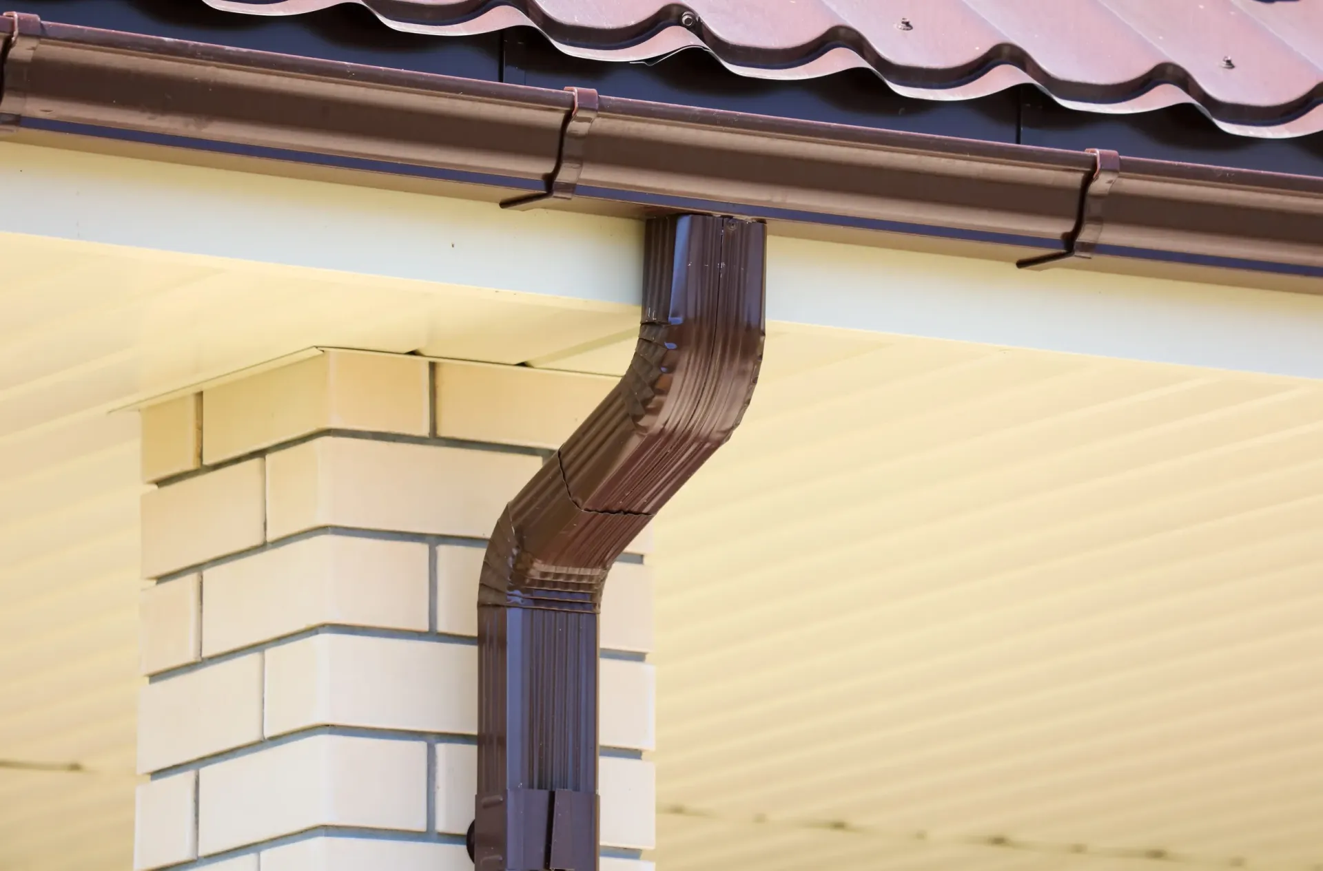 A brown metal gutter system attached to the roofline of a brick house.