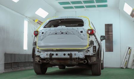 Car's side panel covered with plastic sheeting in a body shop, ready for painting.