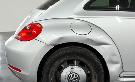 Silver Volkswagen Beetle with a dented rear panel.