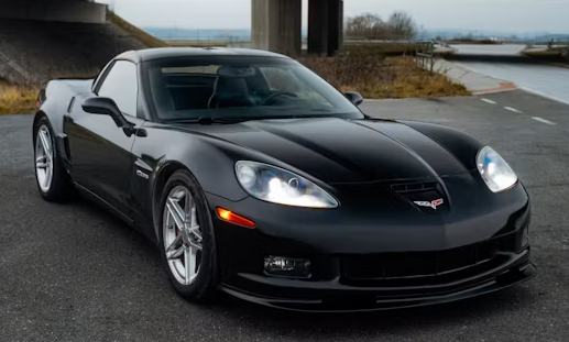 Black sports car parked on a road under a bridge near water and a cloudy sky