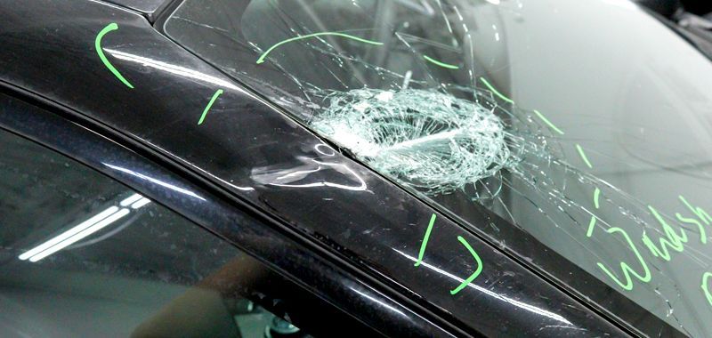 Car windshield shattered from impact. Damage and cracks surround a central point. Green markings are on the vehicle.