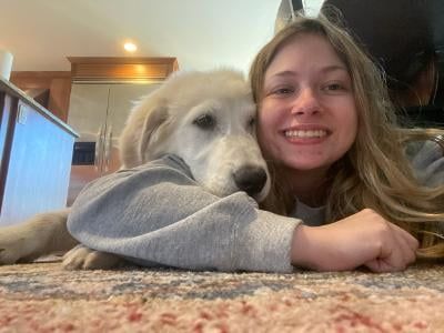 Woman and large white dog lying on a rug, both wearing gray sweatshirts, smiling.