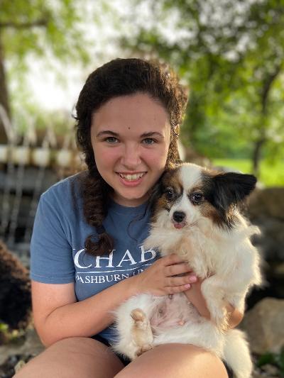 Woman in blue shirt holding a small, fluffy dog, both smiling outdoors.