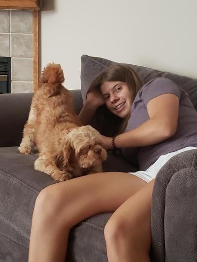 Woman on a couch with a brown dog; woman smiling and petting the dog.