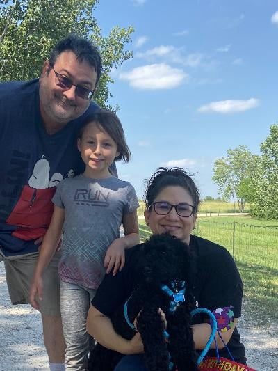 Family outdoors with a black dog on a leash; sunny day.