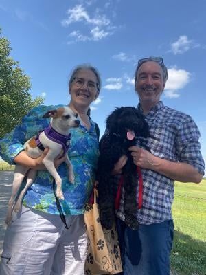 Two people outdoors, each holding a dog. Sunny day.