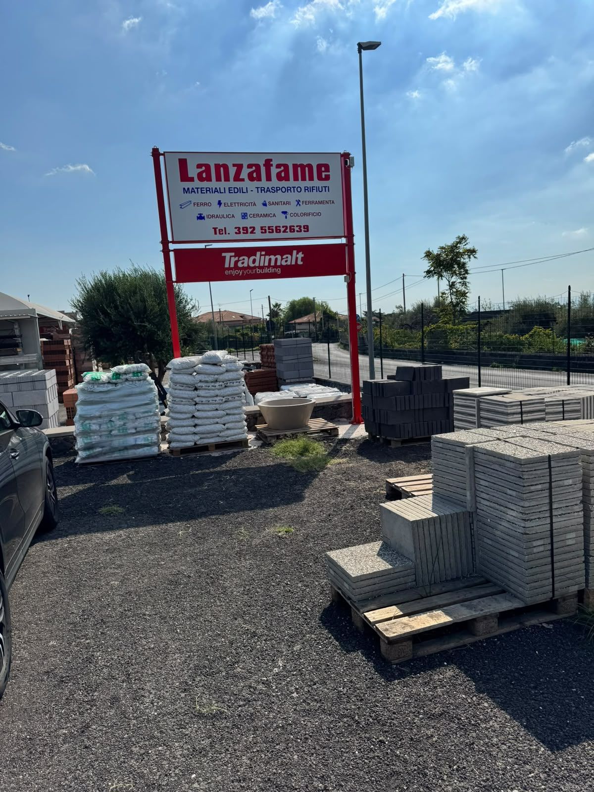Cantiere con cartello Lanzafame, materiali accatastati e pallet su ghiaia, sotto un cielo sereno