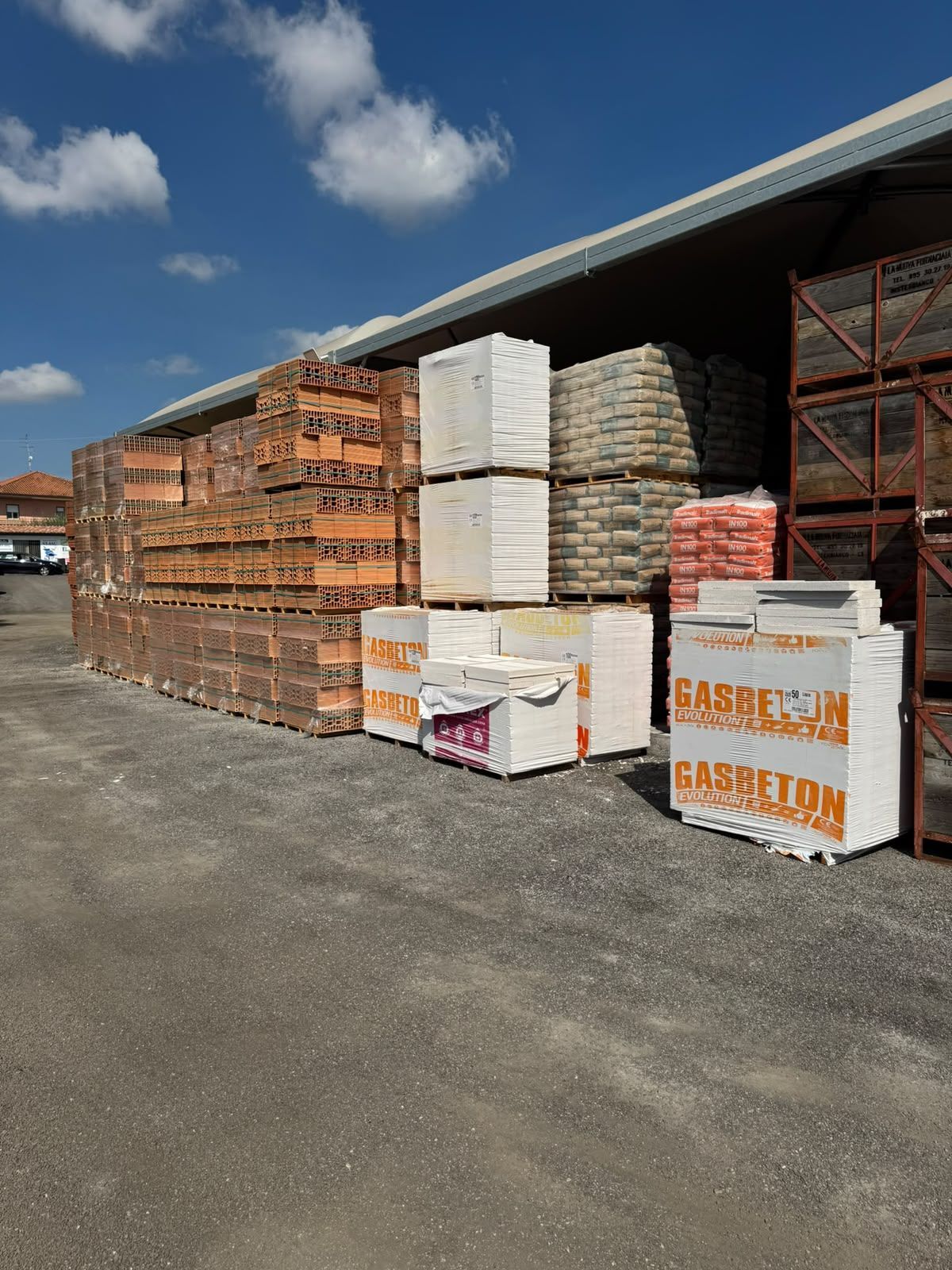 Pile di materiali edili e pallet all’esterno di un magazzino in una giornata di sole
