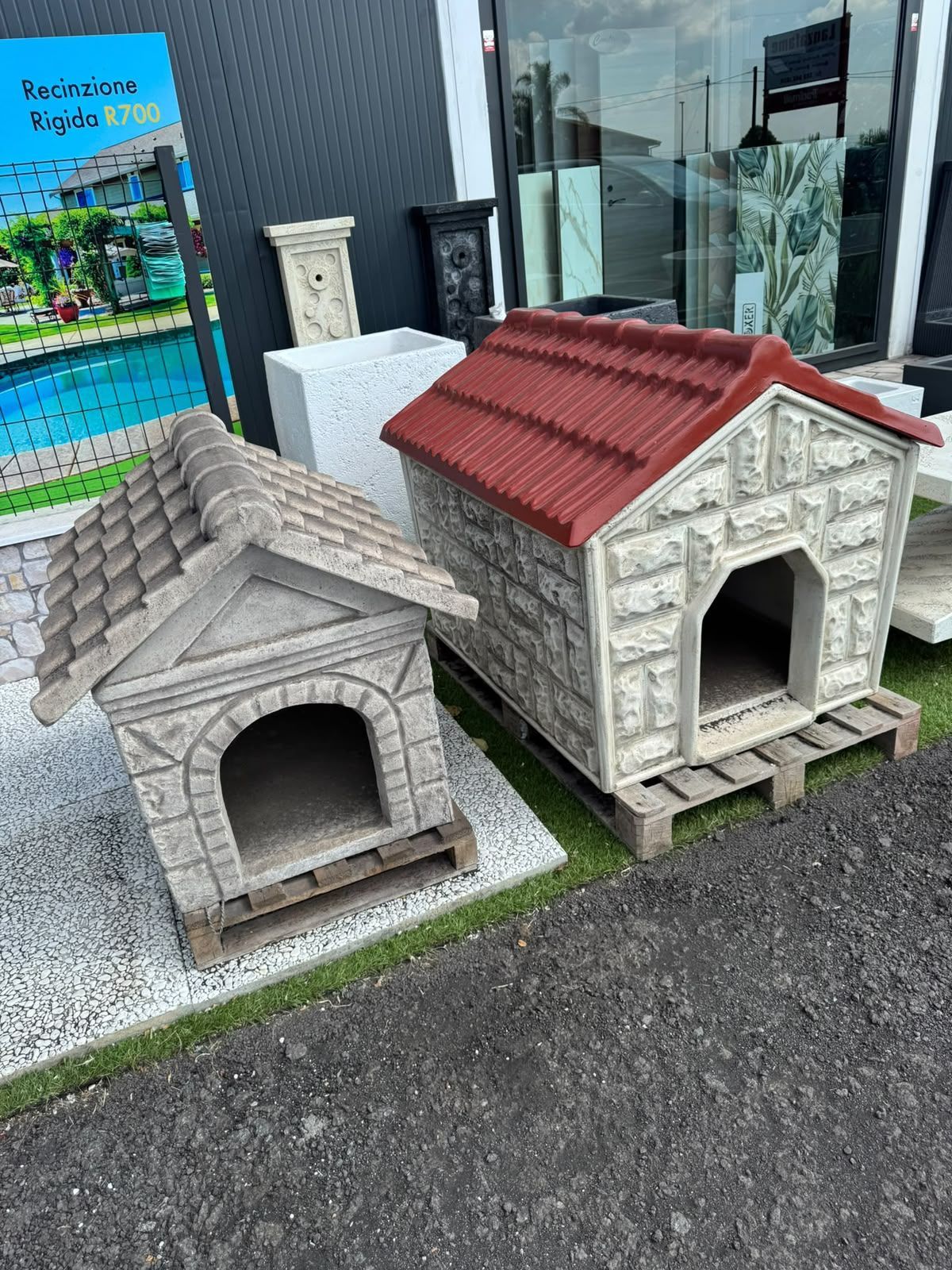 Due casette in pietra per animali domestici, con tetti grigi e rossi, esposte davanti a un negozio