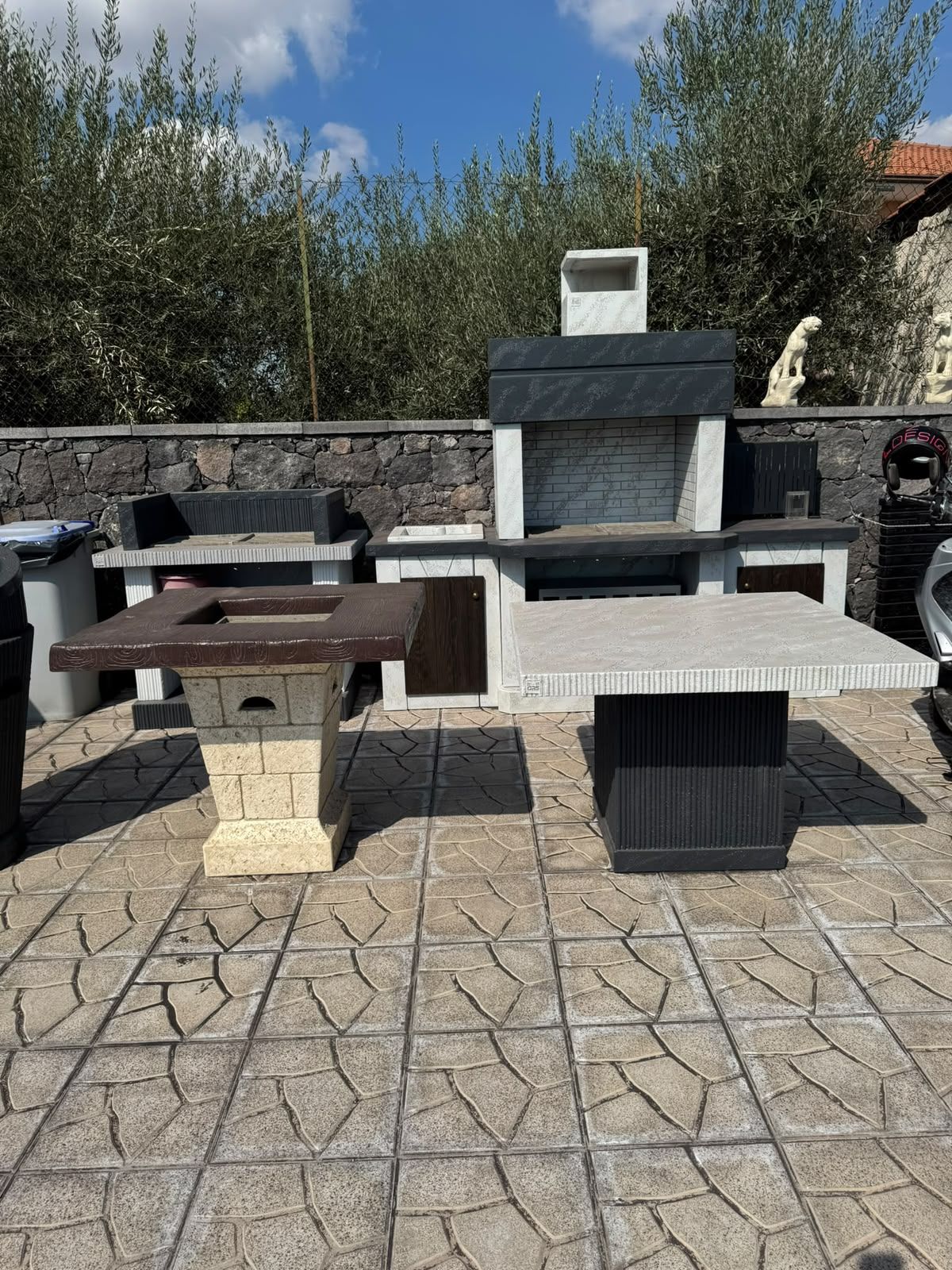Barbecue e area grigliate in pietra all’aperto, con due bracieri in mattoni su un patio pavimentato sotto il cielo azzurro