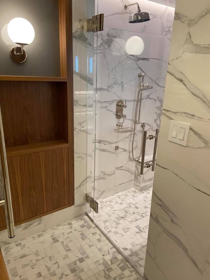 Modern bathroom with marble walls, glass shower, mosaic floor, and wooden shelving unit