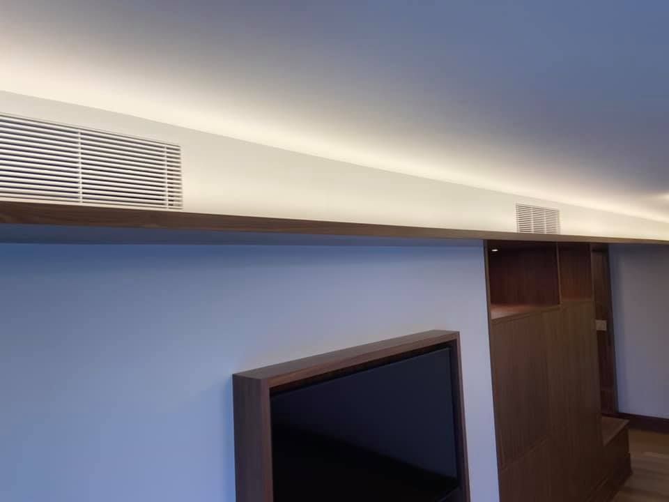 Modern room with blue wall, mounted TV, wood trim, and ceiling vents under soft lighting