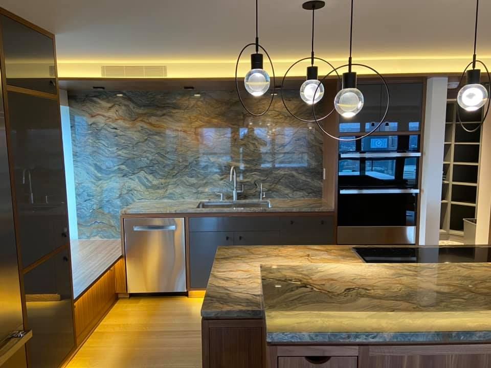 Modern kitchen with stone countertops, pendant lights, stainless appliances, and warm under-cabinet lighting.