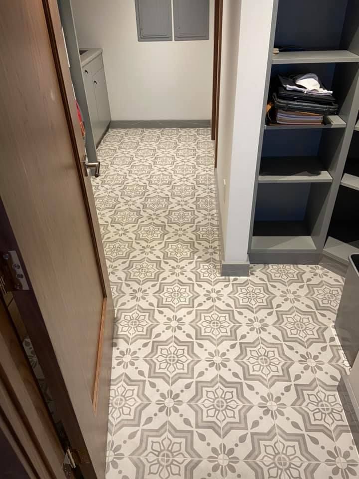 Narrow hallway with patterned tile floor, open door on left, and shelving unit on the right.