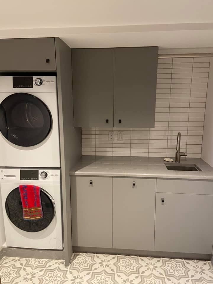 Laundry room with stacked washer and dryer beside gray cabinets, white tile backsplash, and small sink