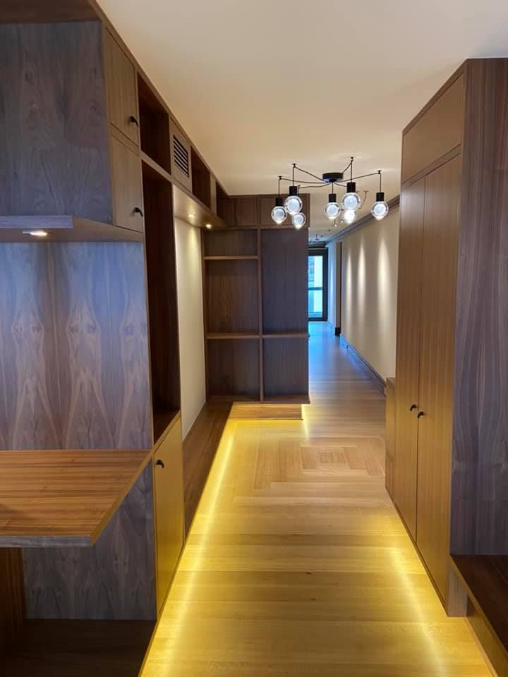 Modern hallway with warm wood built-ins, yellow-lit floor, and pendant lights at the far end
