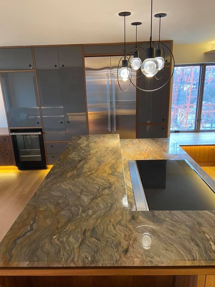 Modern kitchen with large granite island, stainless steel appliances, pendant lights, and sliding glass doors.