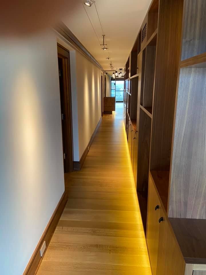 Long wooden hallway with built-in shelving and warm lighting, leading to a bright room at the end