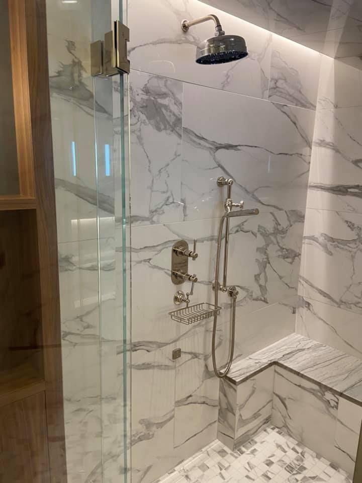 Marble-tiled shower with glass door, brass fixtures, and a built-in bench.