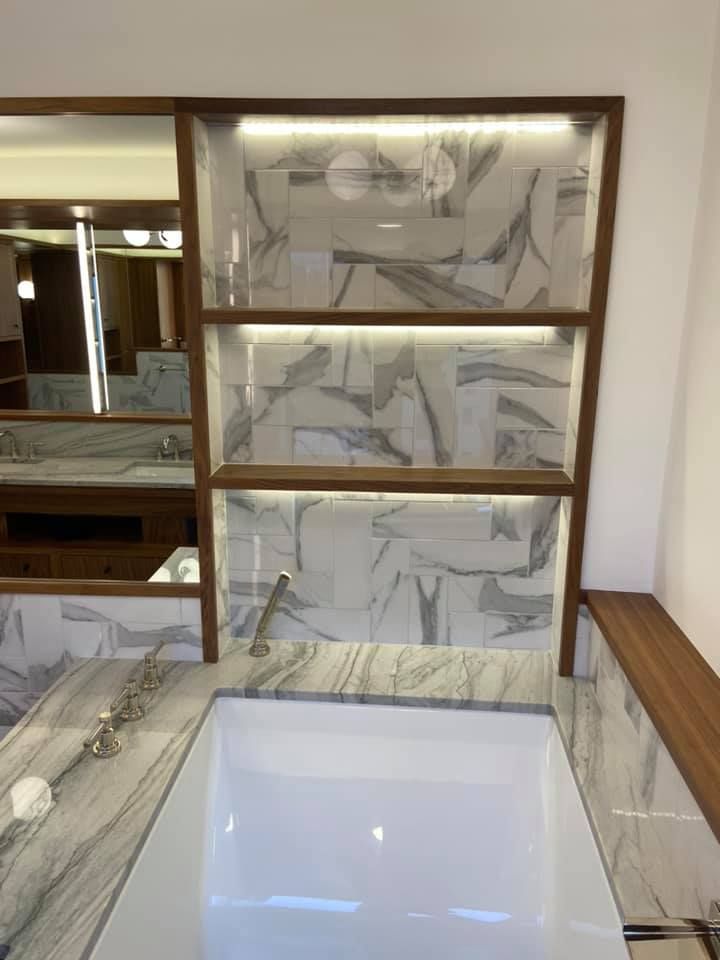Marble bathroom vanity with a white sink, framed mirror, and tiled wall behind it.