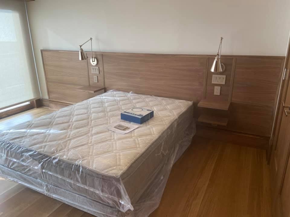 Unmade bed in a simple bedroom with wood headboard and a blue box on the mattress