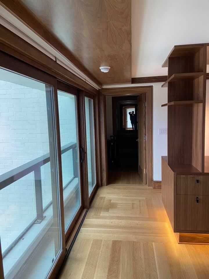 Bright hallway with wood floors, large windows, built-in shelving, and a view into a darker corridor.