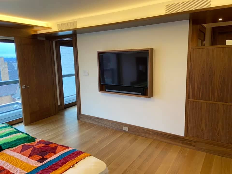 Modern bedroom with wall-mounted TV, wooden floor, and colorful bedspread near large windows