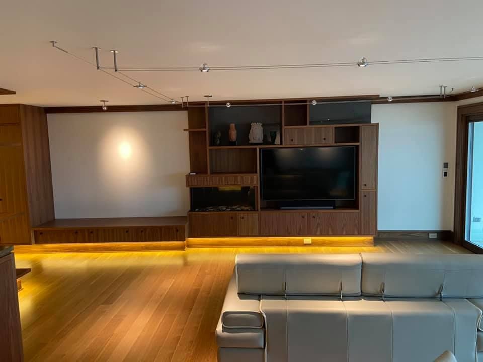 Modern living room with wood-paneled wall, built-in TV, white seating, and soft accent lighting