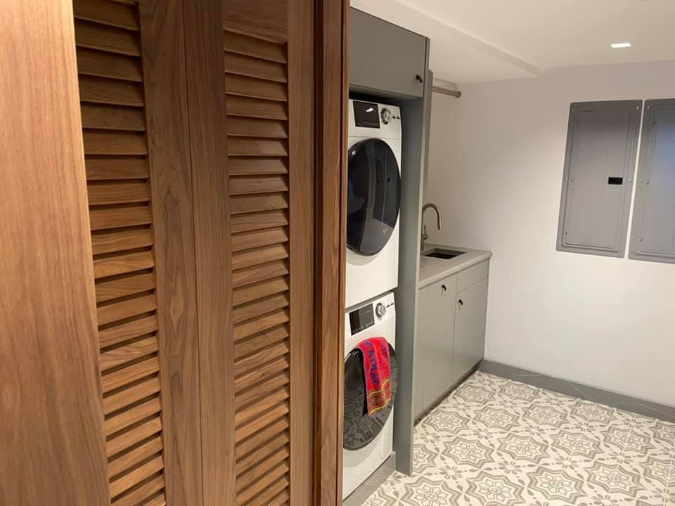 Laundry room with stacked washer and dryer beside a sink, cabinets, and a patterned tile floor.