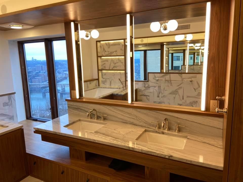 Modern bathroom vanity with double sinks, large mirror, and warm wood finishes, overlooking a view outside