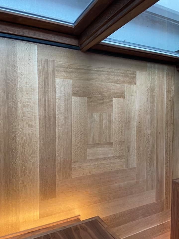 Wood-paneled wall with geometric inlay, lit by warm ambient light beneath skylight windows