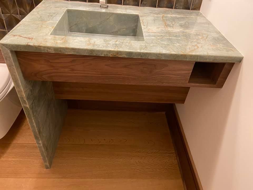 Stone sink vanity with a rectangular basin and open wood cabinet underneath in a small bathroom