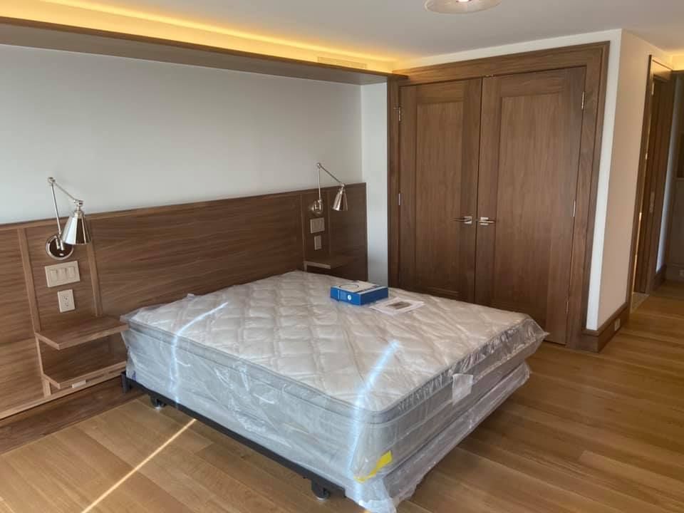 Modern bedroom with a wood bed frame, wrapped mattress, built-in lights, and double closet doors