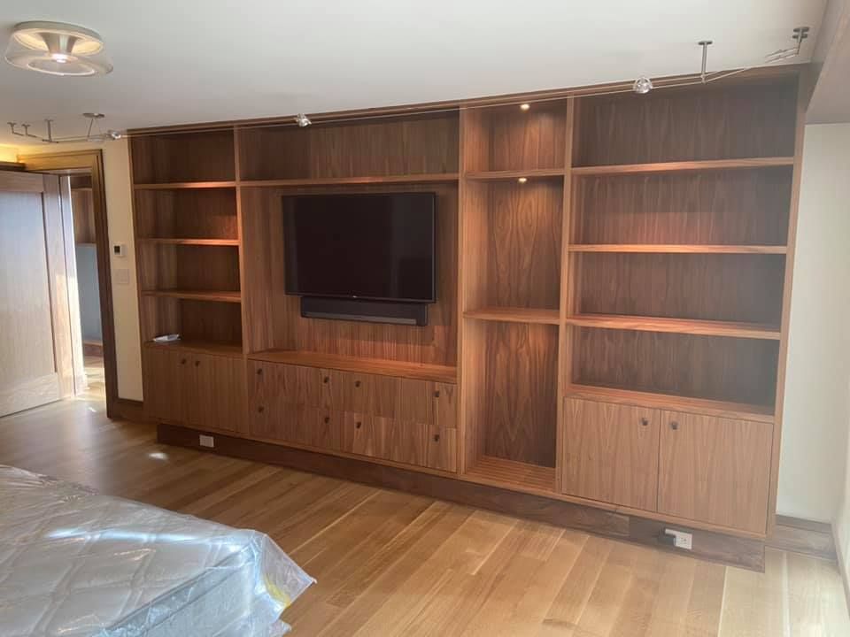 Living room wall unit with built-in wooden shelving and a mounted TV, beside a hardwood floor hallway