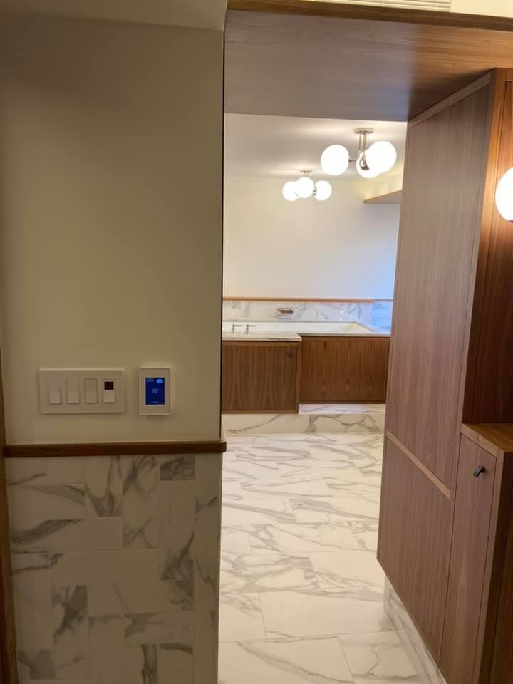Open doorway to a modern bathroom with marble flooring, wood paneling, and a hanging light fixture.