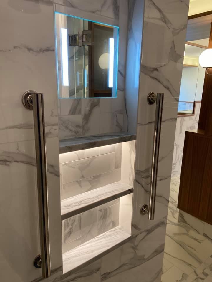 Marble bathroom wall with built-in illuminated shelves, mirror, and chrome grab bars