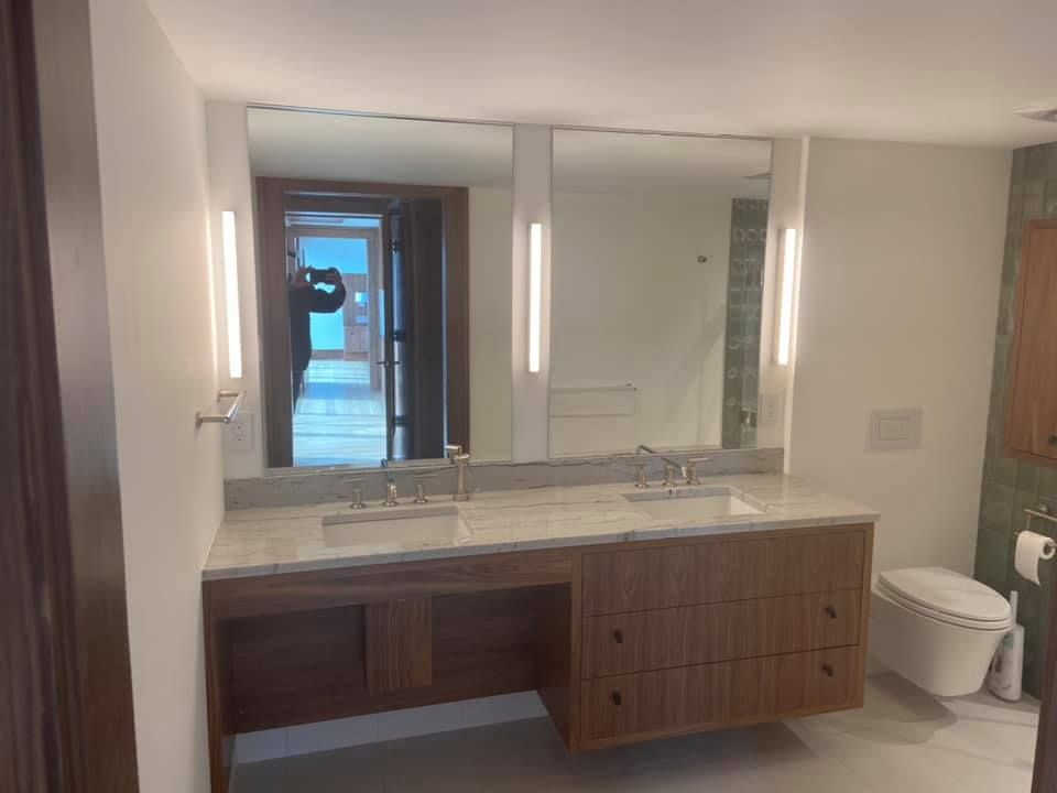 Modern bathroom vanity with large mirror, double sink, wood cabinets, and a toilet on the right.
