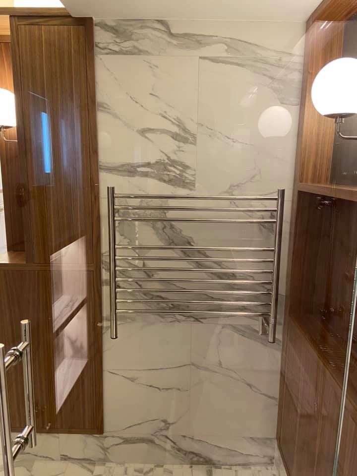 Small bathroom with marble wall, chrome towel rack, wood cabinets, and round light fixtures