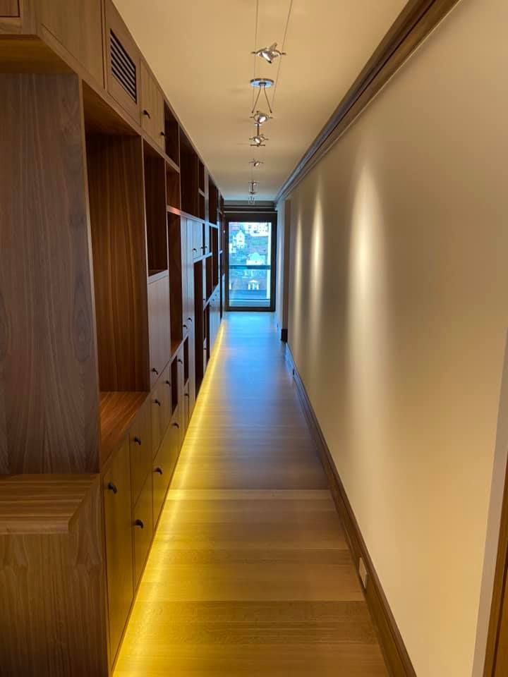 Long narrow hallway with wood shelving on the left, beige wall on the right, and a window at the end.
