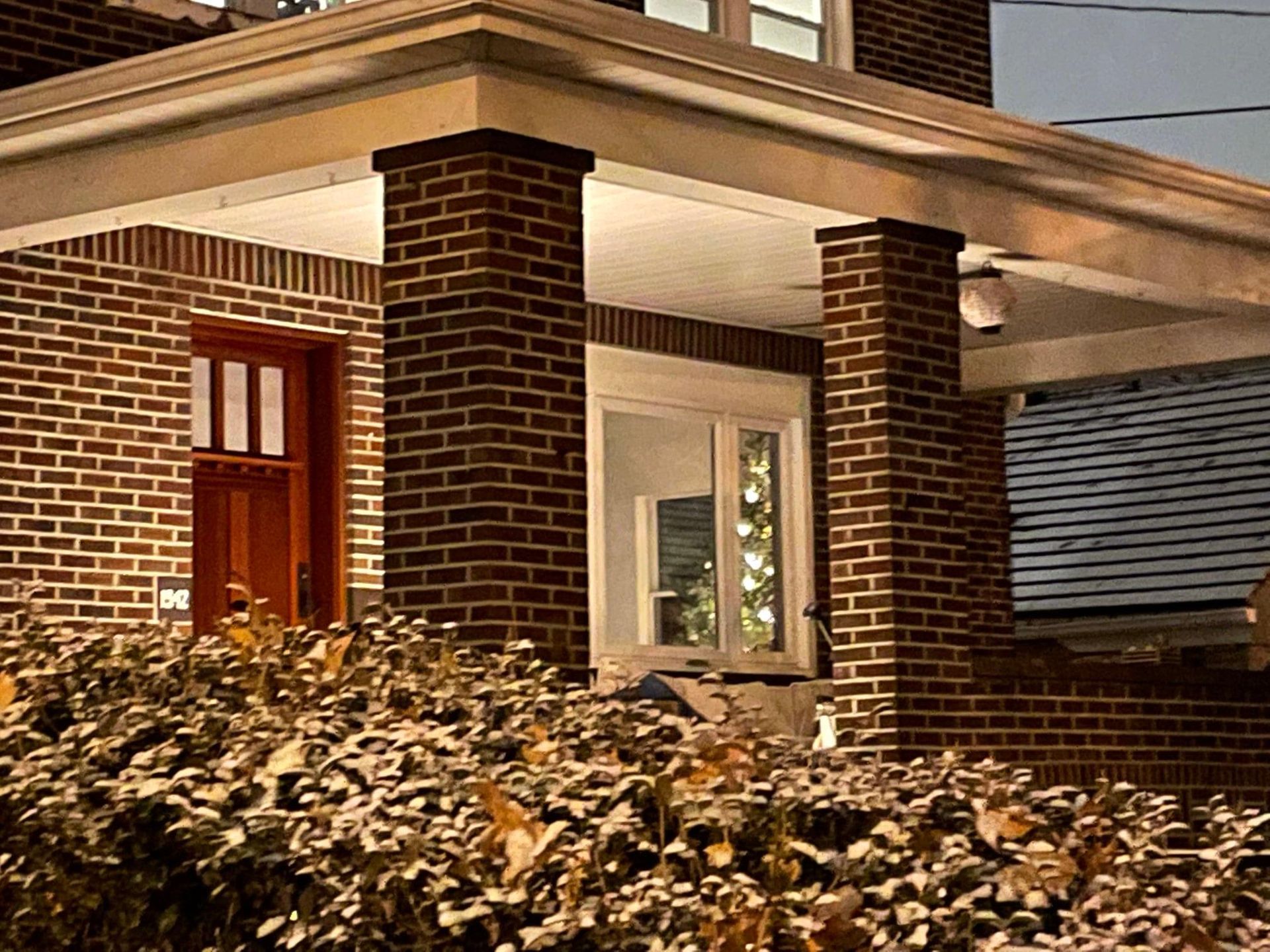 Brick house entrance with a red front door, white trim, and lit porch under a covered roof.
