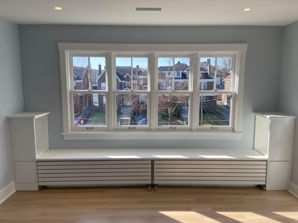 Bright built-in window seat with white drawers beneath a large picture window in a gray room