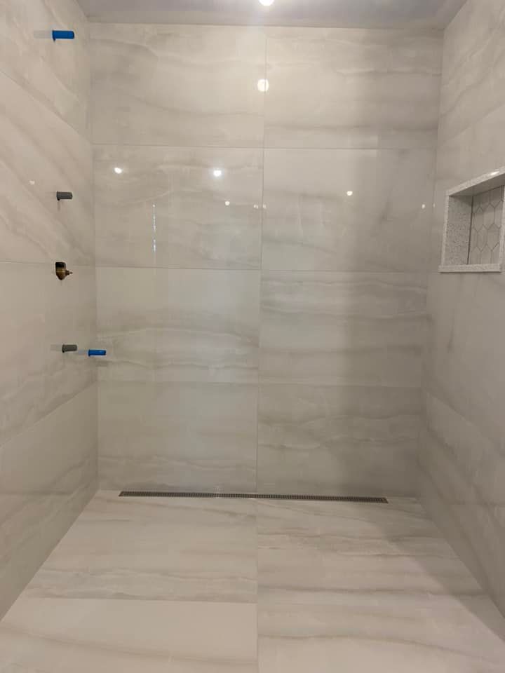 Empty marble-tiled shower with a recessed shelf and glass-door hardware, seen from inside.
