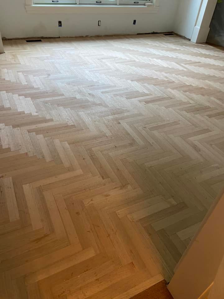 Empty room with light herringbone wood floor and a window at the far wall