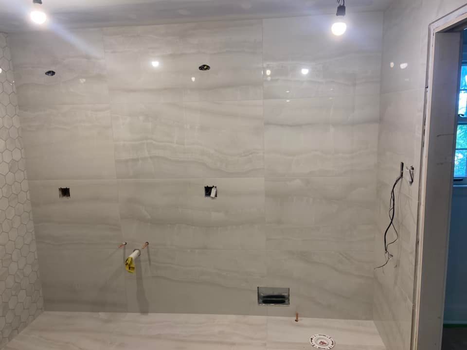 Empty tiled bathroom wall under construction with exposed wires, outlet openings, and ceiling lights.